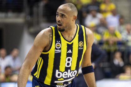 Basketball player in yellow and navy striped jersey with number 8 on the court, spectators in the stands behind him.