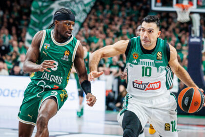 Two basketball players in green uniforms sprint toward the ball during a fast-paced game, crowd in the background.