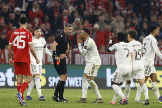 Soccer referee in black talks to a white Real Madrid player while teammates watch during the match