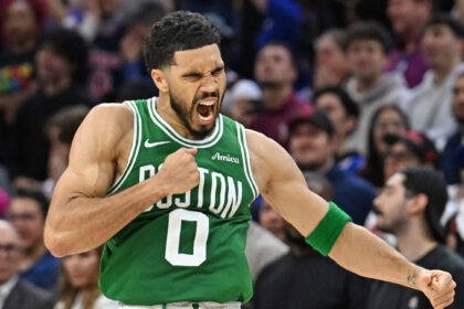 Basketball player in a green jersey with number 0, shouting with a clenched fist during a game, crowd in background.