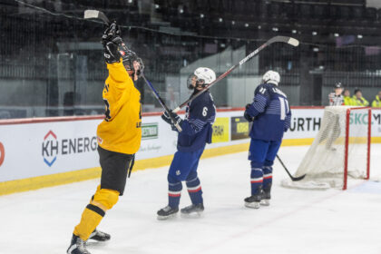 Hockey players on the ice celebrate near the goal; a player in a yellow jersey raises his stick in the air.