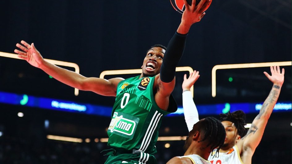 Basketball player in green jersey #0 leaps toward the hoop for a shot while defenders reach up nearby.