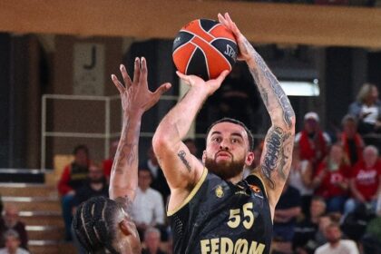 Basketball player in black jersey #55 jumping to shoot the ball over defender in a crowded gym.