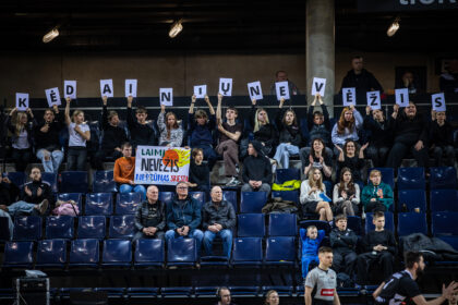 Crowd of spectators in a sports arena holding up letter cards to spell a message across the stands. The signs form a long row above the crowd.