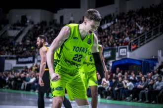 Basketball player in neon green uniform celebrates on court as crowd looks on in a packed arena.