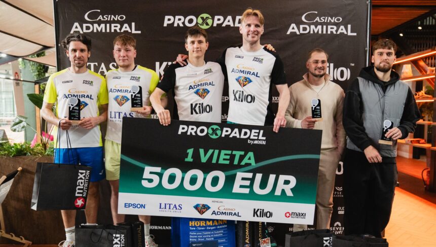Six competitors stand on a podium holding trophies and a large 5,000 EUR prize check, with sponsor banners in the background and black gift bags at their feet.