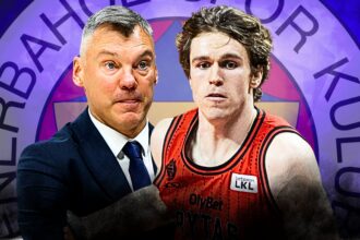 Coach in a dark suit and a basketball player in a red jersey stand side by side in front of a purple circular logo backdrop.