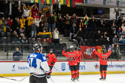 Red-jersey hockey players celebrate a goal on the ice as fans in the stands cheer and wave flags behind them.