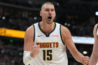 Denver Nuggets player in white jersey #15 celebrates with fists clenched on the court.