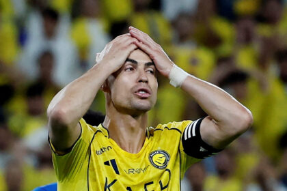 Soccer player in a yellow jersey holds his head in disbelief on the field with a yellow-clad crowd behind him.