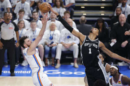 San Antonio Spurs guard in black jersey (number 1) reaches for a ball tipped by Oklahoma City Thunder player in a white jersey as they jump in an arena full of spectators.