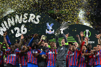 Crystal Palace players celebrate winning a trophy with confetti rain and raised hands on a victory stage.