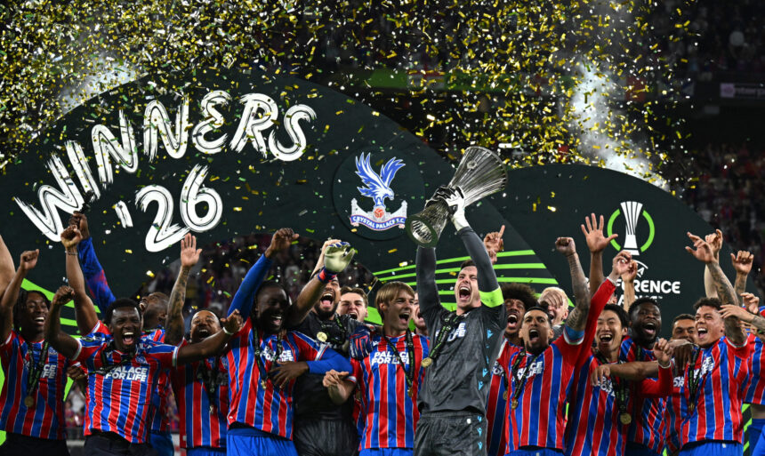 Crystal Palace players celebrate winning a trophy with confetti rain and raised hands on a victory stage.