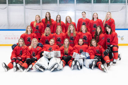 Youth girls' hockey team in red jerseys posing for a group photo on an ice rink.
