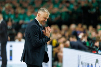 Man in a dark suit bowing with hands pressed together in greeting at a crowded event.