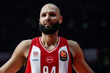 Basketball player with a red-and-white jersey and number 94, arms outstretched on the court.