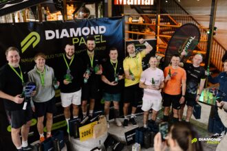 Group of men with medals posing for a photo at a Diamond Padel event, holding beer bottles, with a large 'DIAMOND PADEL' banner and prize bags nearby.