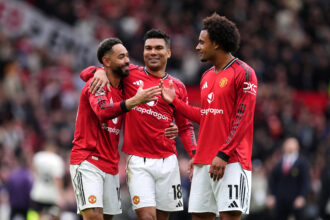 Three Manchester United players celebrate together with arms around each other on the pitch during a match.