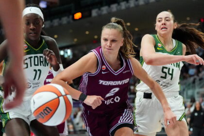 Toronto player in maroon drives for the ball as two defenders in green chase during a fast-paced women’s basketball game.