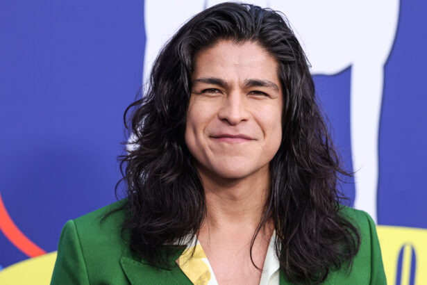Portrait of a woman with long dark hair wearing a green blazer, smiling softly against a blue graphic background.