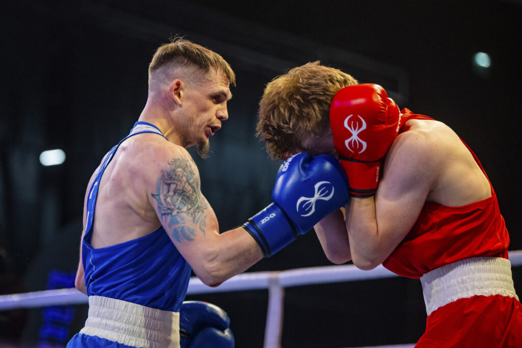 Two male boxers, one in blue and one in red, clash at close range with gloves up in a boxing ring.