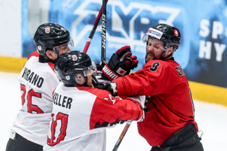 Hockey players in white and red jerseys celebrate on the ice, sticks raised.