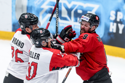 Hockey players in white and red jerseys celebrate on the ice, sticks raised.