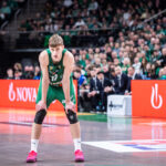 Basketball player in a green jersey bending forward on the court, crowd cheering in the background.