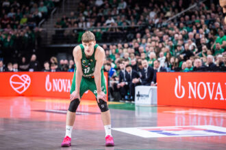 Basketball player in a green jersey bending forward on the court, crowd cheering in the background.