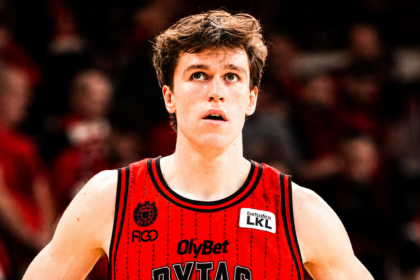 Basketball player in a red jersey, looking upward with a focused expression, crowd blurred in the background