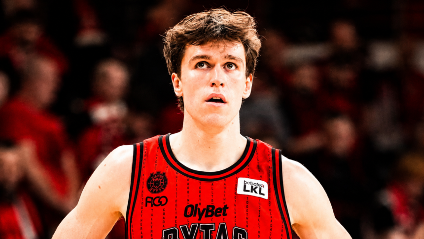 Basketball player in a red jersey, looking upward with a focused expression, crowd blurred in the background