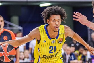 Basketball player in a yellow jersey with #21 dribbling toward the basket as defenders reach in a game.