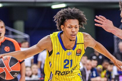 Basketball player in a yellow jersey with #21 dribbling toward the basket as defenders reach in a game.