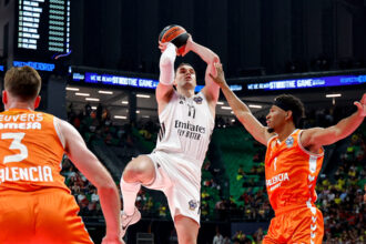 White-clad player soars for a shot as two Valencia defenders in orange contest him in a crowded arena.
