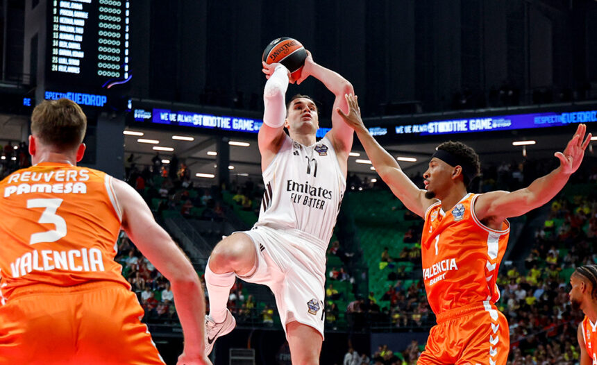 White-clad player soars for a shot as two Valencia defenders in orange contest him in a crowded arena.
