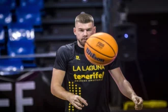 Basketball player in a black La Laguna Tenerife jersey spins an orange ball in a dim arena.