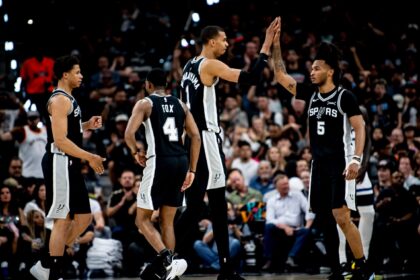 San Antonio Spurs players celebrate with a high-five on the basketball court as a cheering crowd looks on in the background, mid-game.