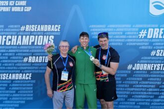 Three male athletes pose with medals in front of a blue backdrop, the center in green holding a medal and bouquet, flanked by two teammates with medals and lanyards.