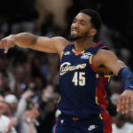 Basketball player in Cavaliers uniform #45 extends arm during game with a cheering crowd in the background.
