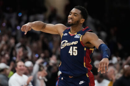 Basketball player in Cavaliers uniform #45 extends arm during game with a cheering crowd in the background.