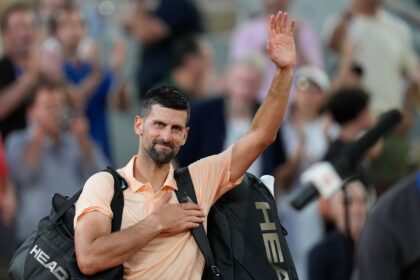 Man waving to the cheering crowd at a sports event, wearing a peach shirt and carrying a HEAD bag.