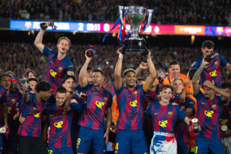 FC Barcelona players celebrate a championship, lifting a large trophy amid cheering fans in the stadium.