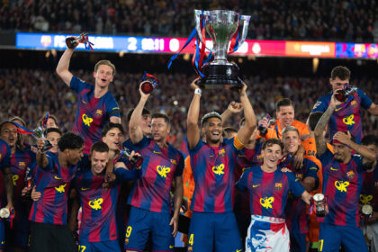 FC Barcelona players celebrate a championship, lifting a large trophy amid cheering fans in the stadium.