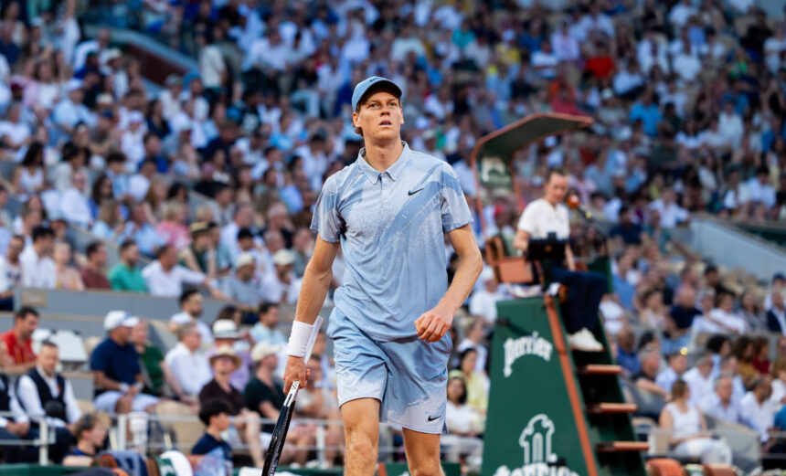 Male tennis player in light blue outfit on court, gazing upward as crowds watch intensely behind him.