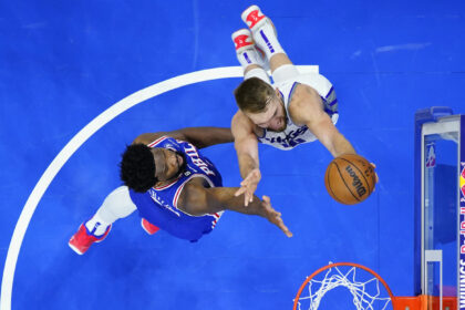 Two basketball players leap for the ball near the hoop on a bright blue court, overhead view of the action.