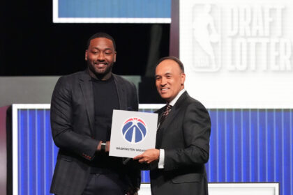 Two men in suits pose on stage holding a certificate with a circular logo; one smiles at the camera.