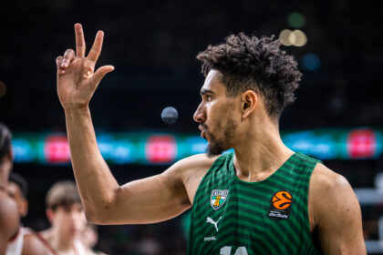 Basketball player wearing a green Žalgiris jersey raises two fingers in a victory gesture on the court.