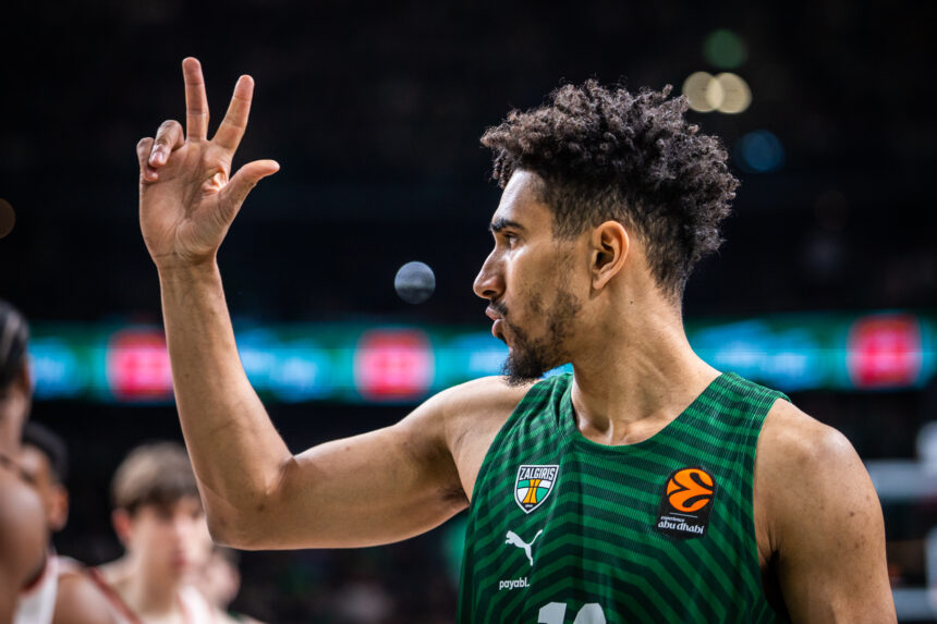Basketball player wearing a green Žalgiris jersey raises two fingers in a victory gesture on the court.