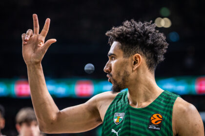 Basketball player wearing a green Žalgiris jersey raises two fingers in a victory gesture on the court.