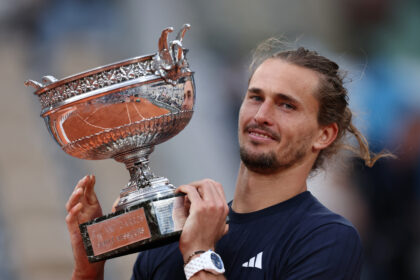 Man holding a large ornate silver trophy up to camera, celebrating victory on court.